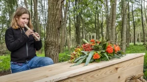 Meisje met een blokfluit in het bos bij een houten grafkist, uitvaart in scene gezet